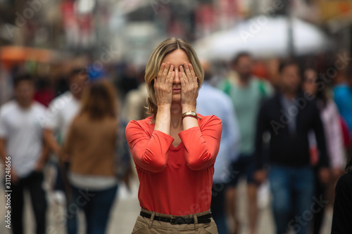 Woman covers his eyes during panic attack in public place. photo