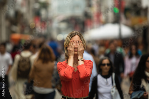 Young woman covers his eyes at standing in the middle of a crowded street.