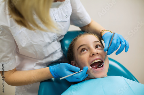 Dentist doing teeth checkup of teen girl in a dental chair at medical clinic.