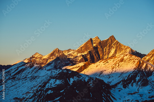 Beautiful nature landscape of Swiss Alps in sunlight rays. Sunset mountains covered with snow in Switzerland. Great view of the snowy rocks and sun beams in Alpine ski resort. Winter holidays.