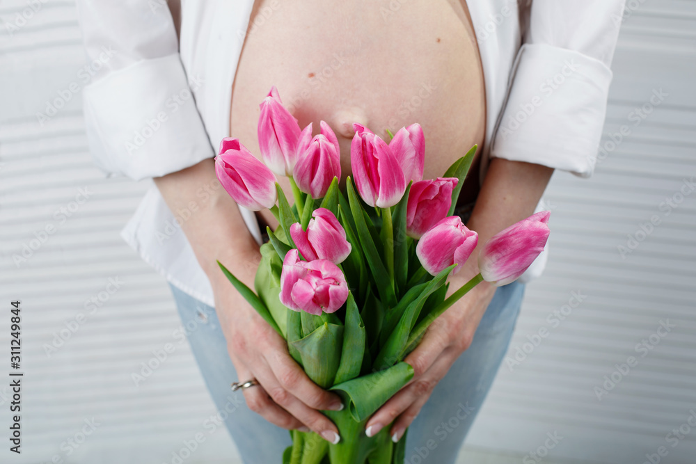  pink tulips in the hands of pregnant girl. portrait a beautiful pregnant woman with flowers close up. young girl hugging her belly. 9 months of pregnancy. woman in anticipation of child birth