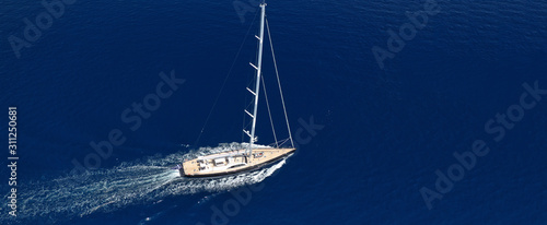 Aerial drone ultra wide photo of beautiful sail boat with wooden deck cruising in open ocean deep blue sea
