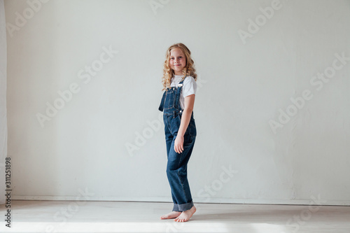 Beautiful little girl in denim jumpsuit played in white room