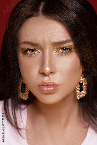 Portrait of beautiful frowns woman with gold smokey eyes perfect tanned skin and gold jewerly