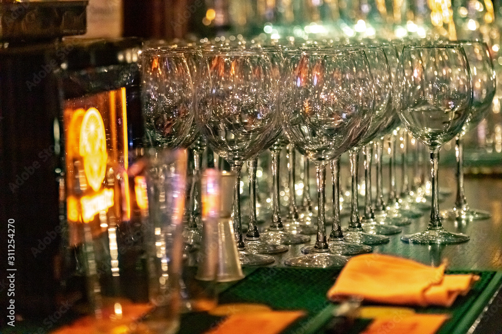 Empty wine glasses on the bar in a dark room, lined up in rows.