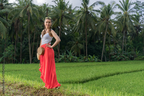 Beautiful young woman in red long maxi skirt with  straw hat and bag. Girl travel in Ubud, Bali, Indonesia © Anna