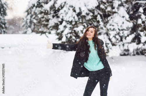 young beautiful girl with loose hair in winter clothes and mittens hitchhiking on the background of snow and forest.