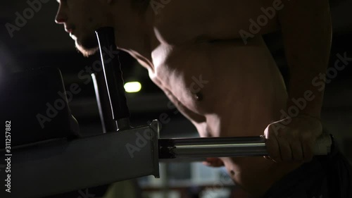 Strong sportsman doing dips on dip-bar in gym to build muscles, close-up workout