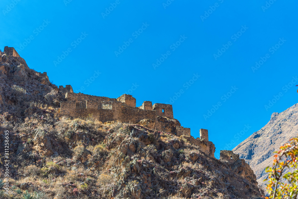 Inca archaeological site with the Sun Temple on the mountain at Ollantaytambo, Peru. Isolated on blue background.