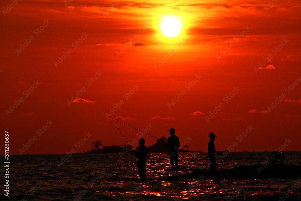 Fototapeta premium Silhouette of fishermans on the beach at sunset