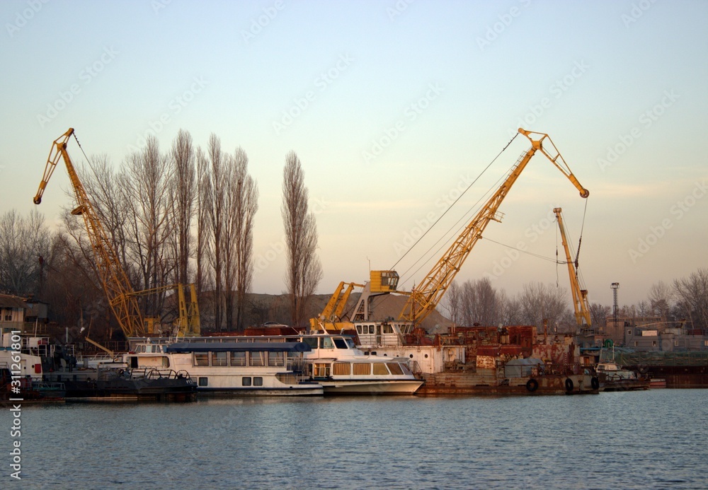 Old yellow cargo cranes in the river port. Nearby are passenger boats.