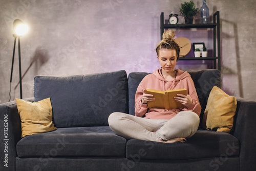 Young girl reading a book. The girl is sitting on the couch. Cozy room.