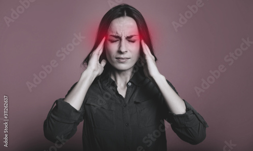 Severe headache. Young stressed woman with eyes closed and her fingers touching temples as a sign of stress or headache.