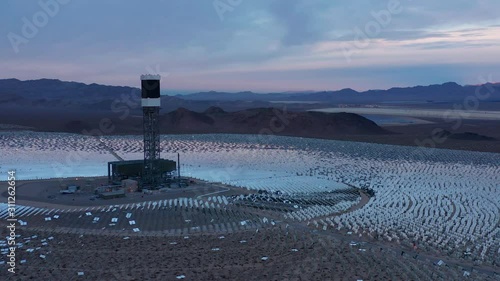 Aerial sunset orbit shot of solar power towers, heliostat mirrors reflections photo