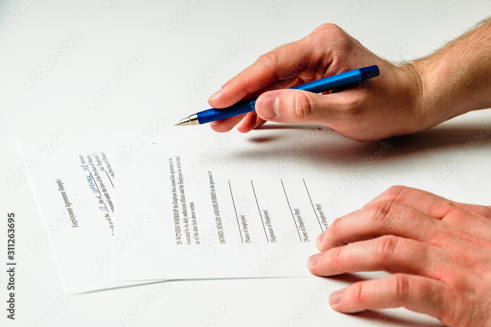 Signing documents. The man is holding a pen and has a contract of employment in front of him. The concept of signing documents and hiring employees. Signing documents. The man is holding a pen and has a contract of employment in front of him. The concept of signing documents and hiring employees.