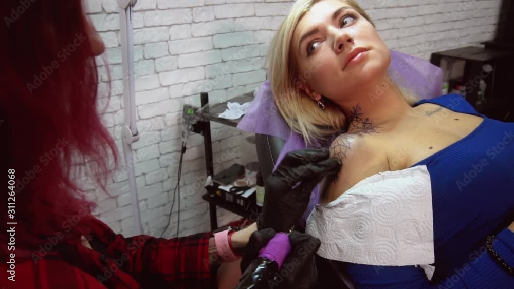 Tatumaster girl with red hair makes a tattoo on the neck in the form of flowers to an attractive blonde woman Tatumaster girl with red hair makes a tattoo on the neck in the form of flowers to an attractive blonde woman