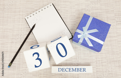 Cube calendar for December 30 and gift box, near a notebook with a pencil photo