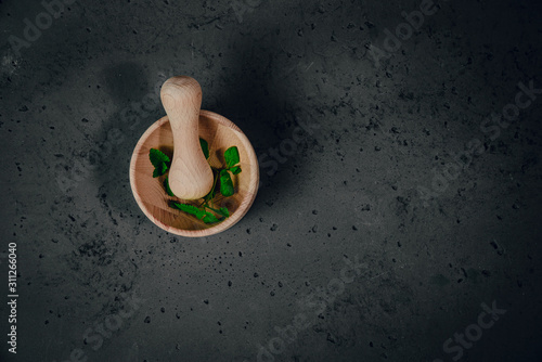 Wooden mortar with herbs on stone background. The concept of crushing and crushing spices, herbs. Preparation of ointments, creams. Caring for health, natural methods of obtaining medicines.