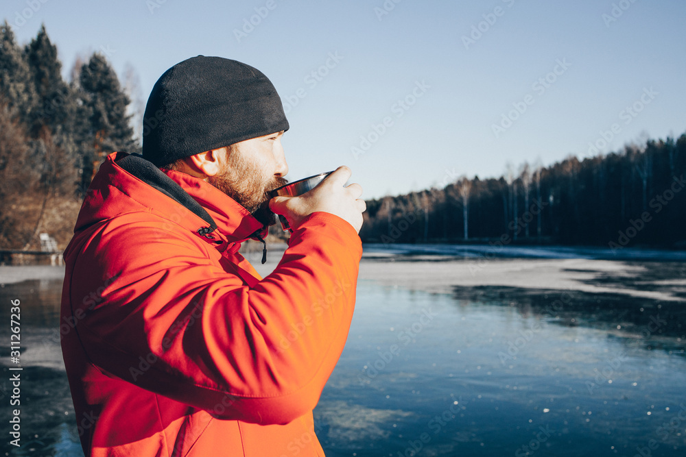 A lone tramp traveler stands on ice and drinks tea from a thermos.