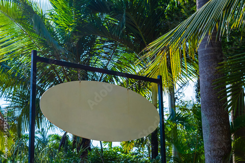 Blank white oval/ circular sign hanging from metal framone stand outdoors under cocut palm trees. Tropical Caribbean island summer sunny weather. Public nature park setting. Welcome entrance signage. photo