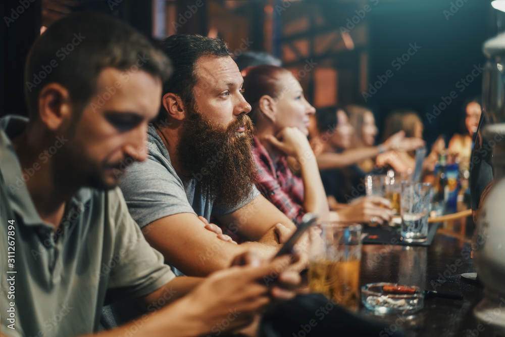 bearded man in crowded bar watching something