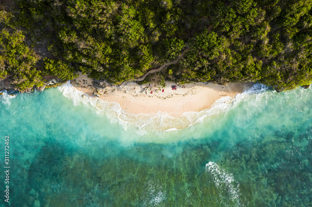 View from above, stunning aerial view of some tourists sunbathing on a beautiful beach bathed by a turquoise rough sea during sunset, Green Bowl Beach, South Bali, Indonesia.