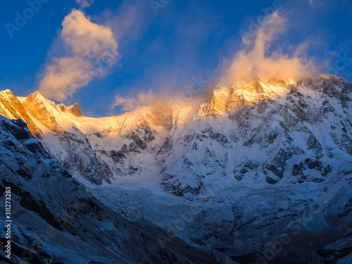 Snow-covered Annapurna South glows in warm sunrise light above a rugged Himalayan valley in Nepal