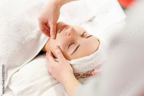 Close up on female woman hands on the face of the young girl giving her relax massage at spa studio relaxing unknown masseur therapist facial therapy treatment caucasian client covered with white
