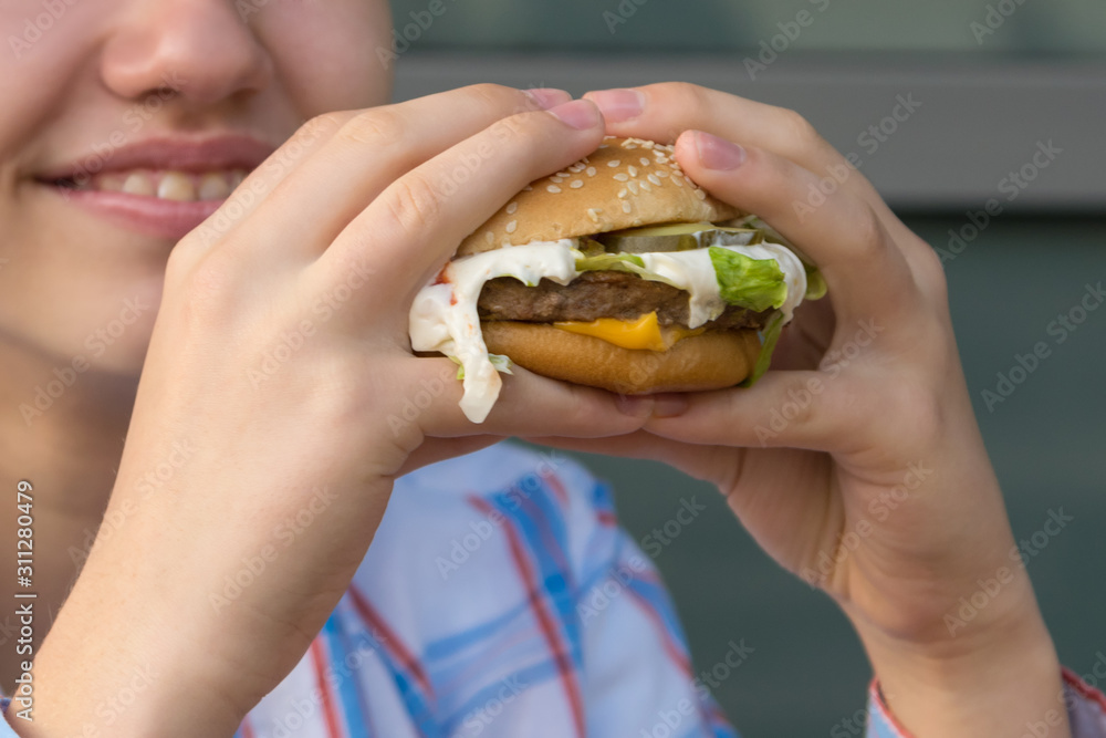 teenager eating a delicious juicy big burger, close-up teenager eating a delicious juicy big burger, close-up