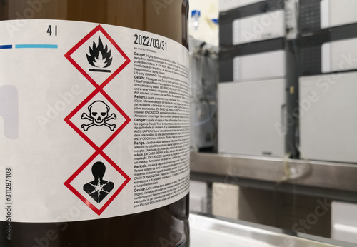 Chemical substance in a laboratory. Amber glass bottle. Tagged with GHS symblogy with toxicity, flammability and death warnings. Liquid chromatography equipment. photo