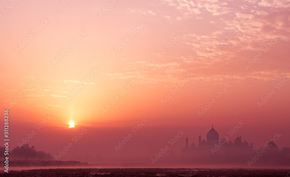 Silhouette of the majestic Taj Mahal temple in the mysterious atmosphere of morning fog at sunrise; bank of the Yamuna river in Agra, India Silhouette of the majestic Taj Mahal temple in the mysterious atmosphere of morning fog at sunrise; bank of the Yamuna river in Agra, India