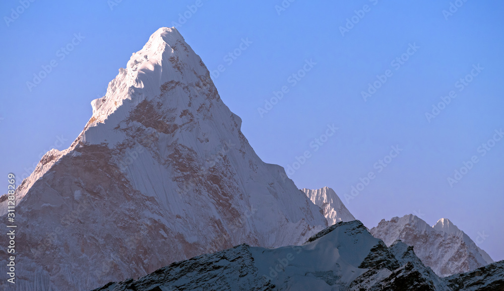 Triangular pyramid of the majestic Ama Dablam (6814 m) peak on the background of blue sky in Nepal, Himalayan mountains; greatness of nature concept
