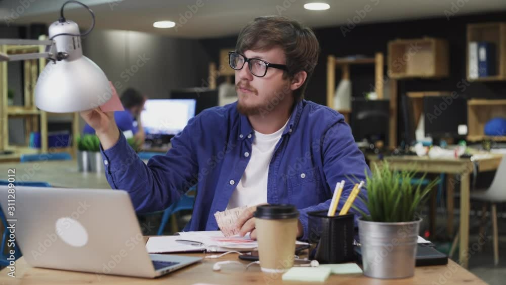 Young man writes notes on sticky multicolored stickers using pen Young man writes notes on sticky multicolored stickers using pen