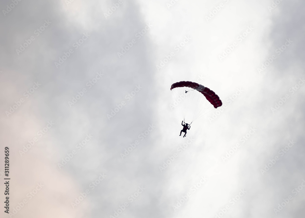 silhouette parachute stunt unfocused and blurry while gliding in the air with red smoke trail during an air exhibition silhouette parachute stunt unfocused and blurry while gliding in the air with red smoke trail during an air exhibition
