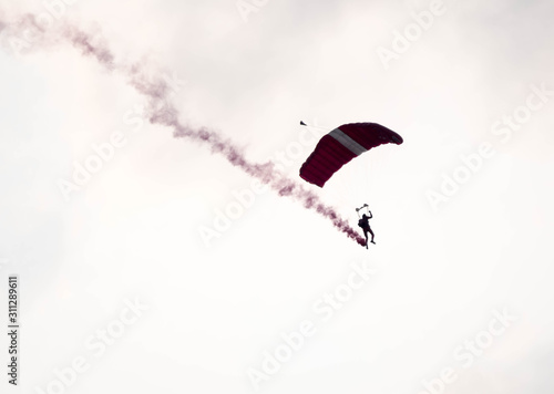 silhouette parachute stunt unfocused and blurry while gliding in the air with red smoke trail during an air exhibition