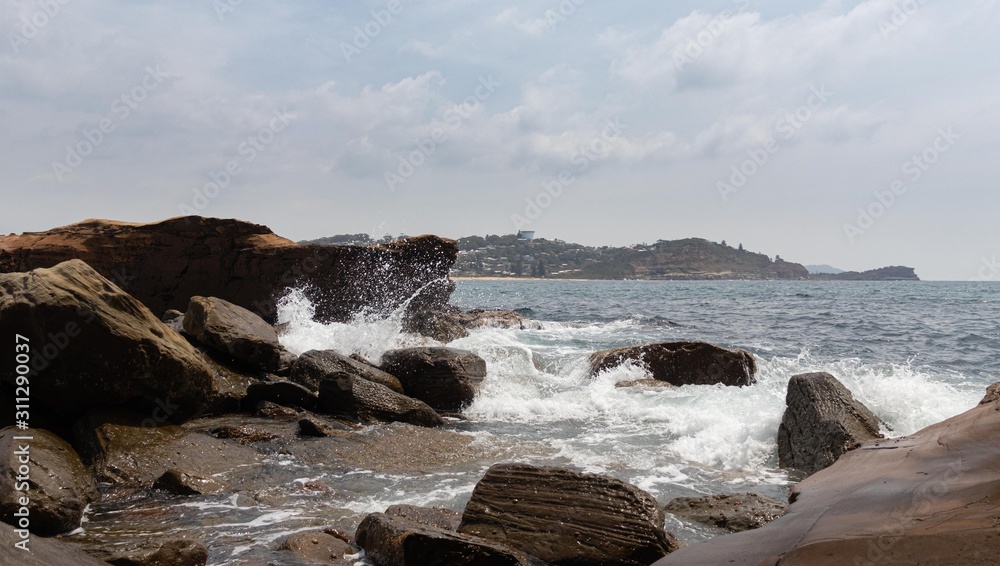 High waves crashing into the rock formations of the beach with many birds and large, pointed rocks.You can see when the wave hits the rock and scatters seawater everywhere.Many drops of water falling.