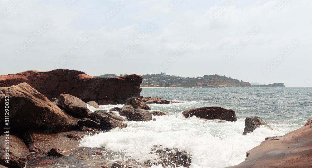 Obraz premium High waves crashing into the rock formations of the beach with many birds and large, pointed rocks.You can see when the wave hits the rock and scatters seawater everywhere.Many drops of water falling.
