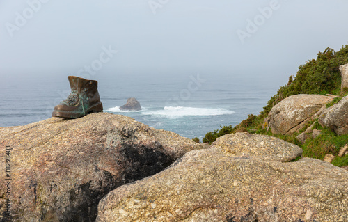 The end of the pilgrimage route in northeastern Spain on the Atlantic Ocean. A hiking shoe stands on a rock above the high cliffs near the town of Finisterre.