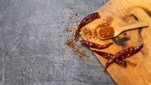 Cayenne pepper in a wooden spoon and dried chillies placed on a wooden chopping board on the cement floor