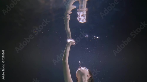 underwater view on swimming woman, stretching hand to surface with her reflection