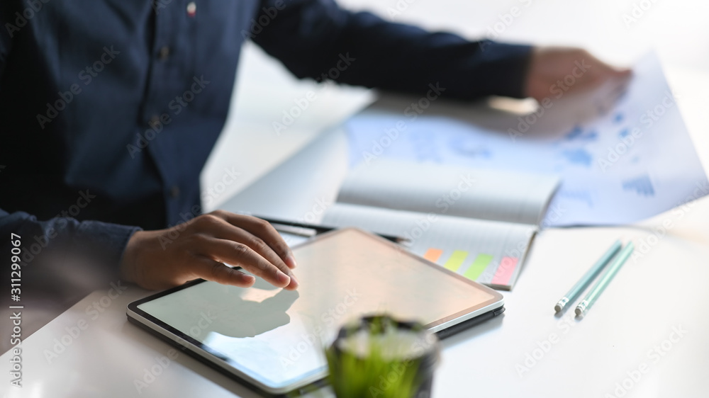 Obraz premium Closeup businessman analysis data with paper report and using tablet computer on table.
