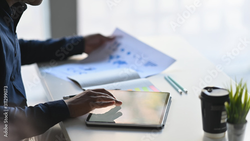 Closeup businessman analysis data with paper report and using tablet computer on table.