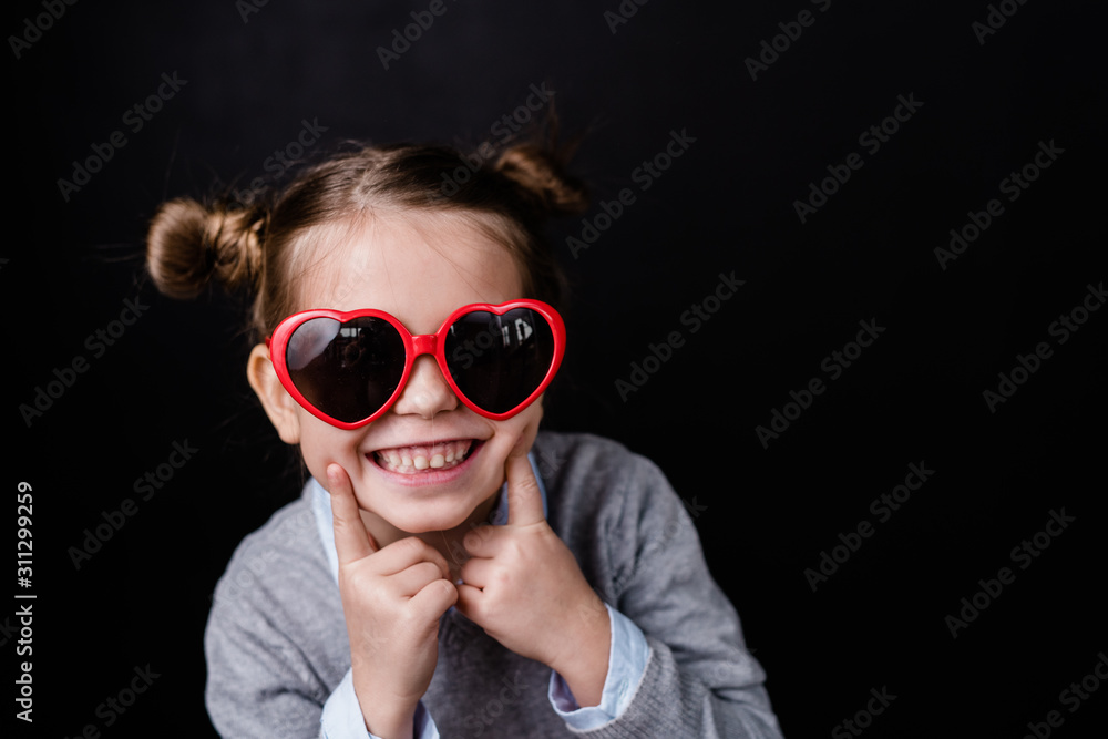 Cute cheerful girl with toothy smile looking through stylish sunglasses