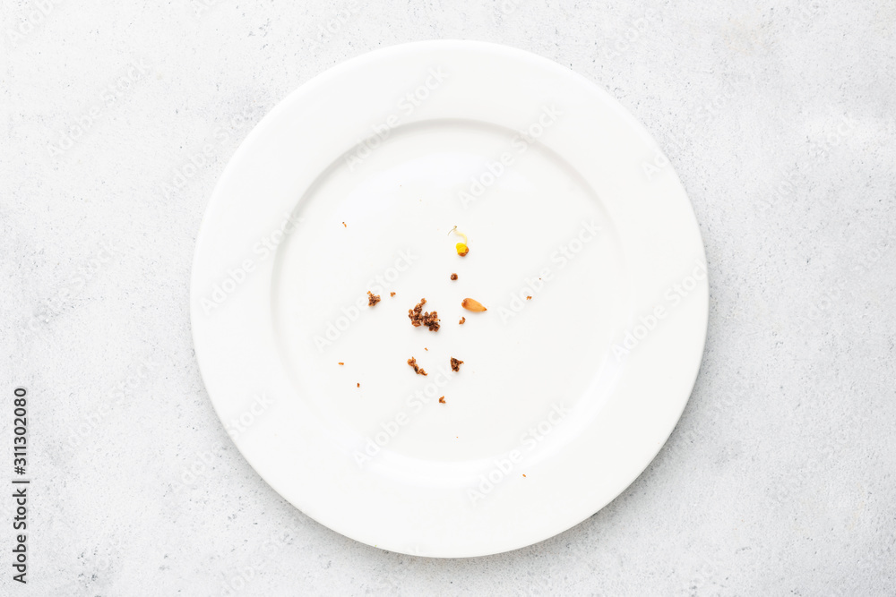 White plate with crumbs leftovers on grey concrete background. Top view White plate with crumbs leftovers on grey concrete background. Top view