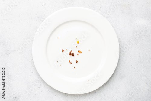 White plate with crumbs leftovers on grey concrete background. Top view photo