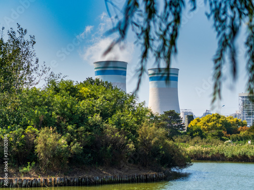 Cooling towers / smokestacks of a nuclear power plant spewing white smoke seen from within a public park. To illustrate pollution and the dangers of nuclear power
