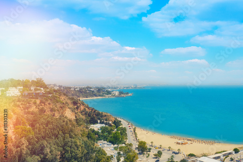 Fototapeta Naklejka Na Ścianę i Meble -  Top view of the beach, sea and coastal road to the city in Sidi Bou Said, Wallpaper background. Mediterranean seascape, Tunisia. June 2019