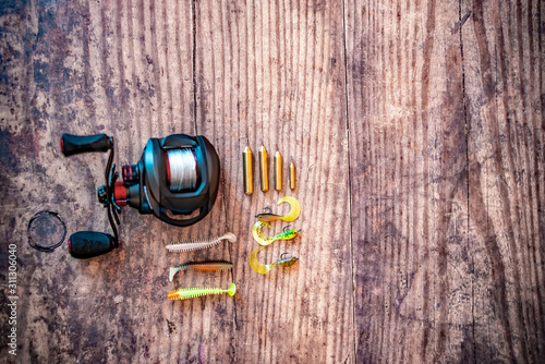  Selective focus on drop shot lures together with a soft focus bait caster fishing reel on a plain wooden background