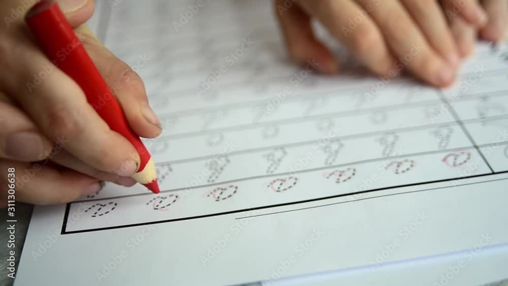 Father teaching child to write letters on handwriting sheets with his hands. Red pencil, grey background Father teaching child to write letters on handwriting sheets with his hands. Red pencil, grey background