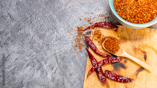 Cayenne pepper in a wooden spoon and blue cup with dried chillies placed on a wooden chopping board on the cement floor background.